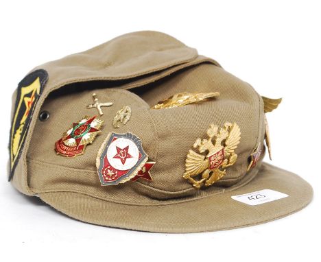 A Russian military cap with date numerals to the inside, having several gilt metal and enamel badges pinned to the hat