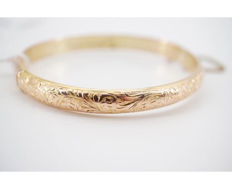 A 9ct gold hinged bangle, with foliate engraved face, engraved 'E Emmerson' to the interior, 8.1g (a/f)