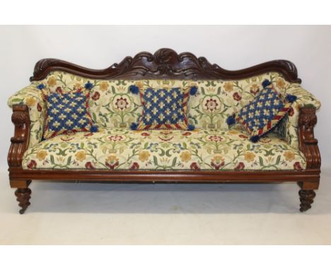 Good early Victorian mahogany and crewel work upholstered sofa of large size, with heavily carved arched back and swept arms,