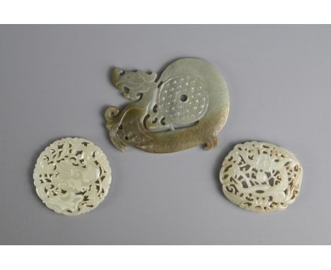 THREE CHINESE JADE PENDANTS. To include a circular carved and pierced pale celadon pendant depicting fish in a lotus pond; An