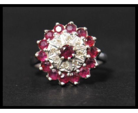 A hallmarked 18ct white gold ruby and diamond cluster ring having a central raised ruby in claw setting surrounded by eight i