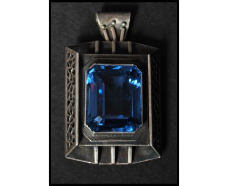 A Liberty style white metal brooch pendant having set with a large blue stone having a stylised pendant bale and roller clip 