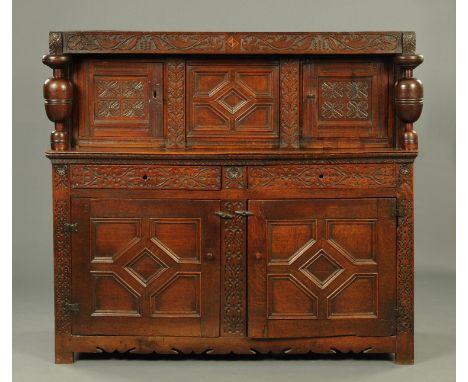 A 17th century oak court cupboard, with carved frieze above a series of panelled doors and shelf flanked by turned columns an