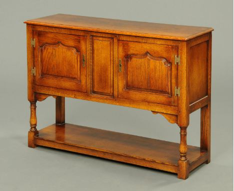 An oak sideboard, with moulded edge above a pair of panelled cupboard doors with turned legs and low shelf.  Width 106 cm.  C