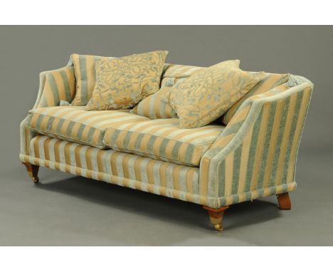 A large lounge settee, upholstered in velvet and linen striped material, with loose cushions and raised on wooden legs termin