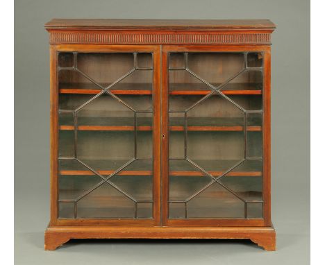 An Edwardian mahogany glazed low bookcase, with moulded edge above a fluted frieze and with pair of glazed doors beneath with