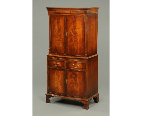 A Reprodux mahogany cabinet, having a moulded cornice to the serpentine front fitted with a pair of panelled cupboard doors, 