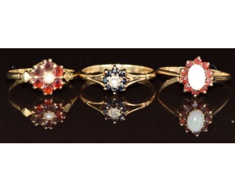 Three 9ct gold rings set with an opal surrounded by garnets, a pearl surrounded by garnets and a diamond surrounded by sapphi