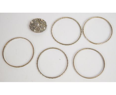 Five Libyan silver bangles with floral and circular decoration and a white metal brooch