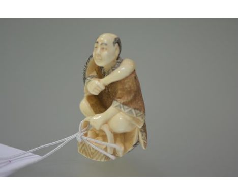 A Japanese ivory netsuke carved as a street vendor, a basket at his feet, holding a scoop, two character mark to base. 52mm