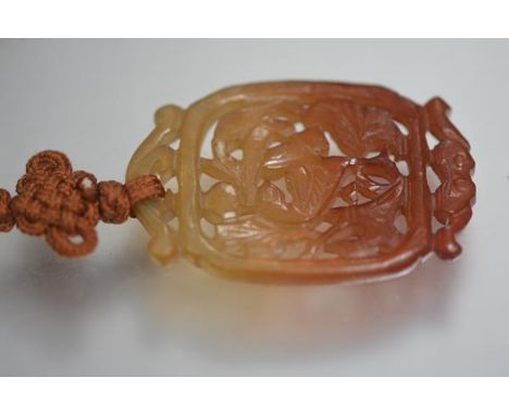 A Chinese russet jade pendant, the panel pierced and carved as a bird, on a silk neck chain. Pendant 50mm by 35mm