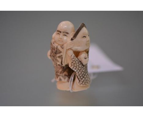 A Japanese ivory netsuke, carved as a man and a child playing with a mask, inscribed to the base. 47mm