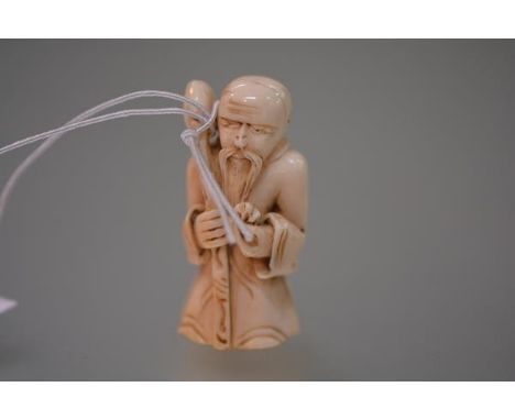 A Japanese ivory netsuke, carved as a sage carrying a staff. 49mm