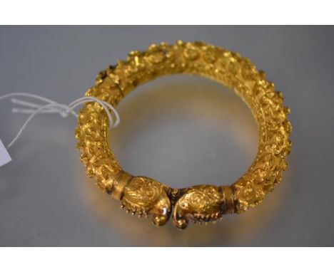 An Indian yellow metal hinged bangle, probably high carat gold,  with exotic beast terminals, the band with leaves and flower