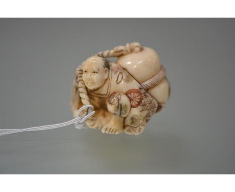 A Japanese ivory netsuke, carved as a crouching vendor under the weight of a large sack, decorated with bamboo and flowerhead