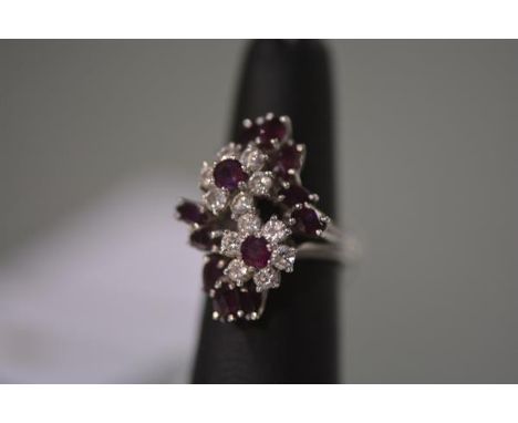 A diamond and ruby cluster ring, set with twin diamond flowerhead clusters, each with central round-cut ruby surrounded by te