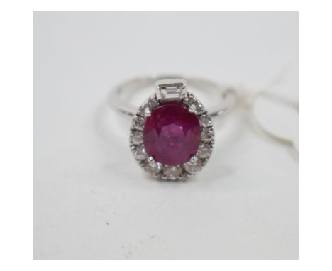 A white coloured metal ruby and diamond cluster ring, the central cushion cut ruby surrounded by brilliant and a baguette cut