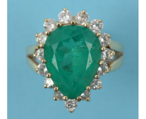 An emerald and diamond cluster ring, the central pear cut emerald surrounded by 15 brilliant cut diamonds, in a yellow colour