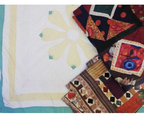 A white ground quilt with green and yellow border and flower design, and two pieces of quilted fabric, mixed textiles of vari