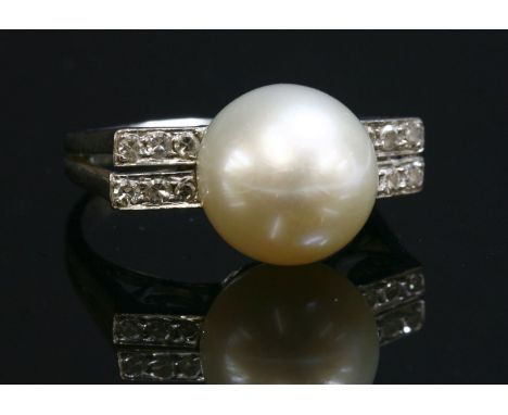 A single stone cultured pearl ring with diamond set shoulders, c.1935-1940, a cultured pearl, 10mm diameter, cup and peg set 