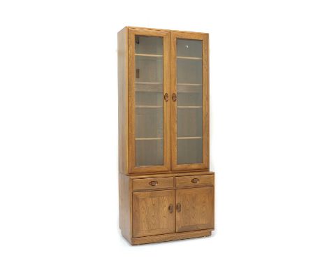 An Ercol elm 'Windsor' display cabinet, with pair of glazed door enclosing teak fronted glass shelves, raised on a base with 