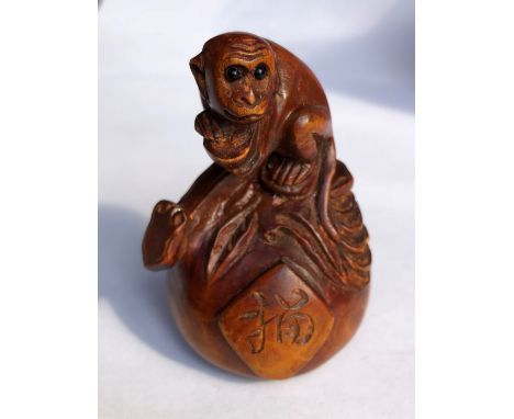 JAPANESE WOOD CARVED NETSUKE OF A CROUCHING MONKEY ON A GOURD.