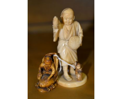 Ω A Japanese Walrus Ivory Okimono, depicting a man standing atop a tree stump whilst playing a shamisen, a boy dances around 