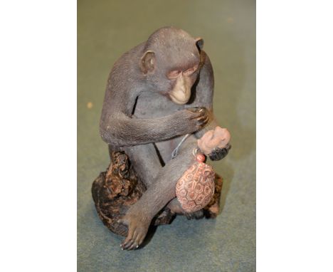A Japanese Pottery Model of A Macaque,  the simian sits cross-legged whilst holding a kinchaku and its netsuke in one hand, t