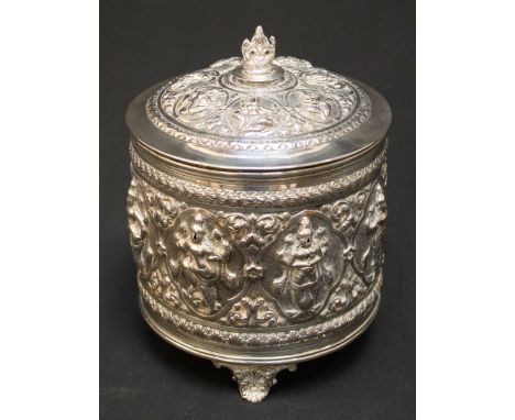 An early 20th century Indian white metal repoussé biscuit barrel, ornately embossed all over with deities, scrolls and flower