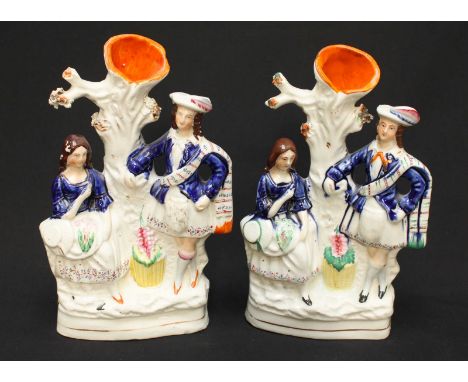 Two Victorian Staffordshire pottery figures each modelled as a highland boy and girl, standing beside a tree trunk. 24 cm hig