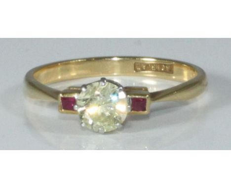 An 18ct gold ring eight claw set with a solitaire diamond and a rubover set with a small ruby to each shoulder. The round bri