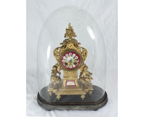 An ornate gilt spelter mantel clock, the case with floral finial and red dial with Roman numerals denoting hours, flanked by 