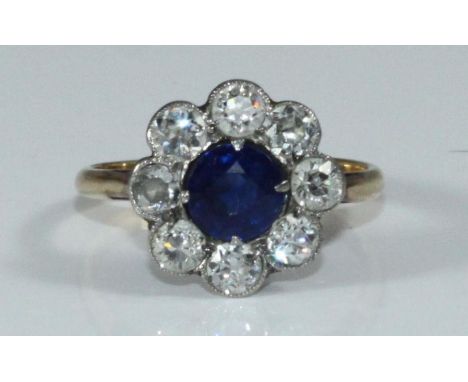 A unmarked yellow metal diamond and sapphire cluster ring, centrally set around- facetted sapphire, surrounded  by eight roun