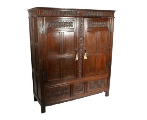 A Late 17th/Early 18th Century Carved Oak Press Cupboard, the fielded panel doors enclosing pegs and a later brass rail, thre
