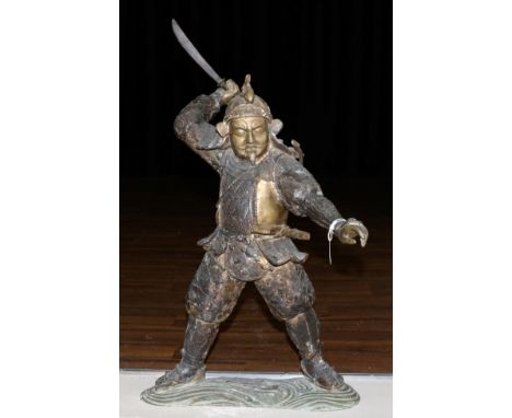 A Japanese Bronze Figure of a Samurai, Meiji period, standing holding a short sword in his raised right hand, on a wave form 