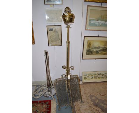 An early 20th Century brass floor standing oil lamp, the reservoir held by scrolling supports on extending stem and scrolling