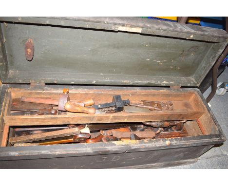 A pine box with fitted handles to either side, containing woodworking tools, including: saws; planes; chisels; a drill; etc.