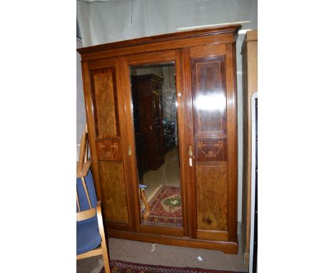 An Edwardian inlaid mahogany three door wardrobe, the dentil cornice above a central bevelled mirror panel door, two further 