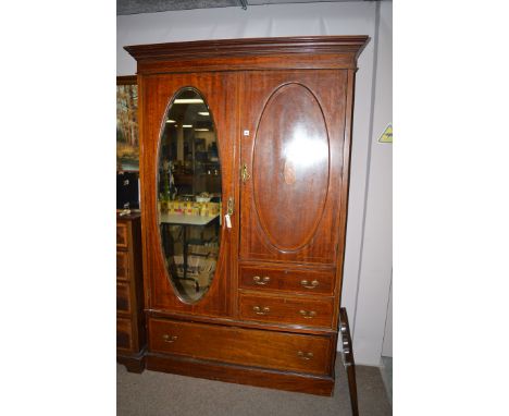 An Edwardian mahogany mirror front wardrobe, the oval mirror panel door enclosing hanging space, further hanging to right-han