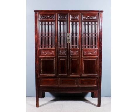 A Chinese stained wood and panelled cabinet with moulded cornice, fitted one shelf and four drawers, enclosed by a pair of fr