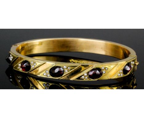 A late Victorian 15ct gold stiff bangle set with garnet and seed pearl, the five oval cut garnets, each approximately .75ct b