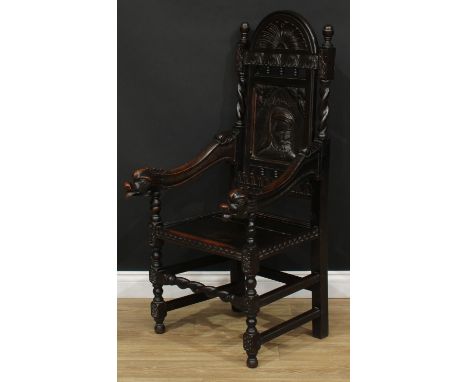 A late 19th century oak 'Wainscot' style open armchair, arched cresting carved with a stylised floral lunette, the back panel