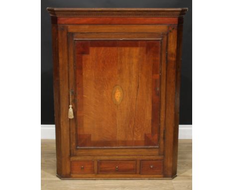 A George III oak and mahogany splay front wall hanging corner cupboard, rectangular panel door inlaid with an oval shell pate