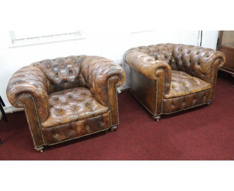 A pair of leather upholstered and button back chesterfield style club armchairs on small brass castors, with brass stud work 