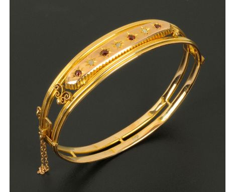 A late Victorian 9 ct gold bangle, set with three diamonds and four ruby coloured stones, with safety chain, 8.2 grams (see i
