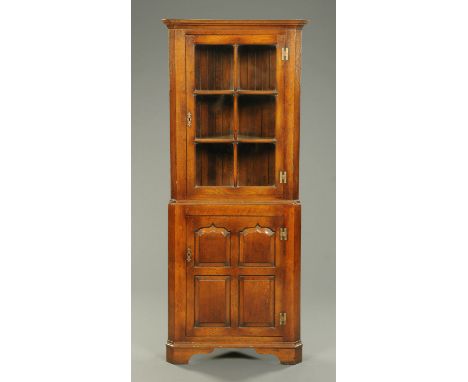 A reproduction oak corner cabinet, with glazed upper door and panelled lower door and raised on bracket feet.  Width 73 cm. 