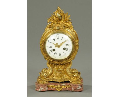A 19th century French brass mantle clock, with two-train striking movement, with dolphin supports and raised on a pink marble