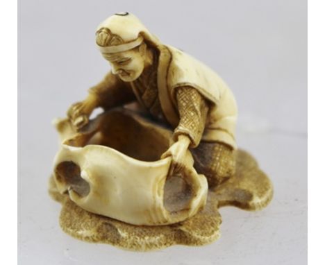 A JAPANESE MEIJI PERIOD CARVED IVORY NETSUKE in the form of a kneeling man, cloth in hand, cleaning an amorphic bowl, bears c