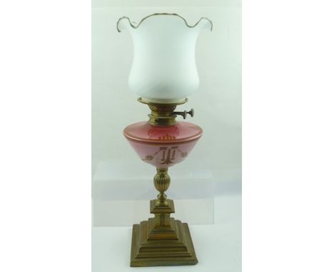 A LATE VICTORIAN OIL LAMP with decorative pink glass reservoir on a brass pedestal and stepped base, together with an opaque 