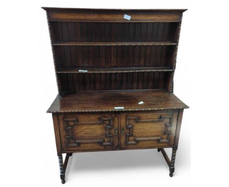 A circa 1930s/'40s oak dresser with shelved top above pair of panelled doors enclosing shelved cupboard and bobbin supports; 